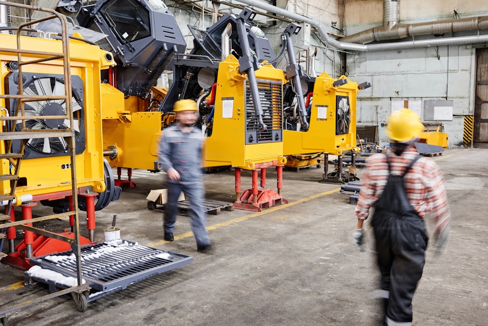 Movimiento borroso de dos trabajadores de la planta industrial que caminan a lo largo de un taller espacioso con filas de máquinas enormes y otros equipos