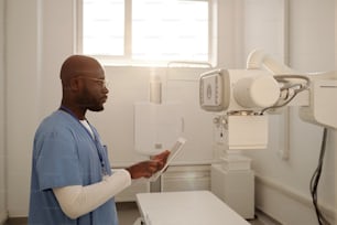 医療機器の前に立ちながらタブレットのX線装置の設定を選択するアフリカ系アメリカ人の男性臨床医