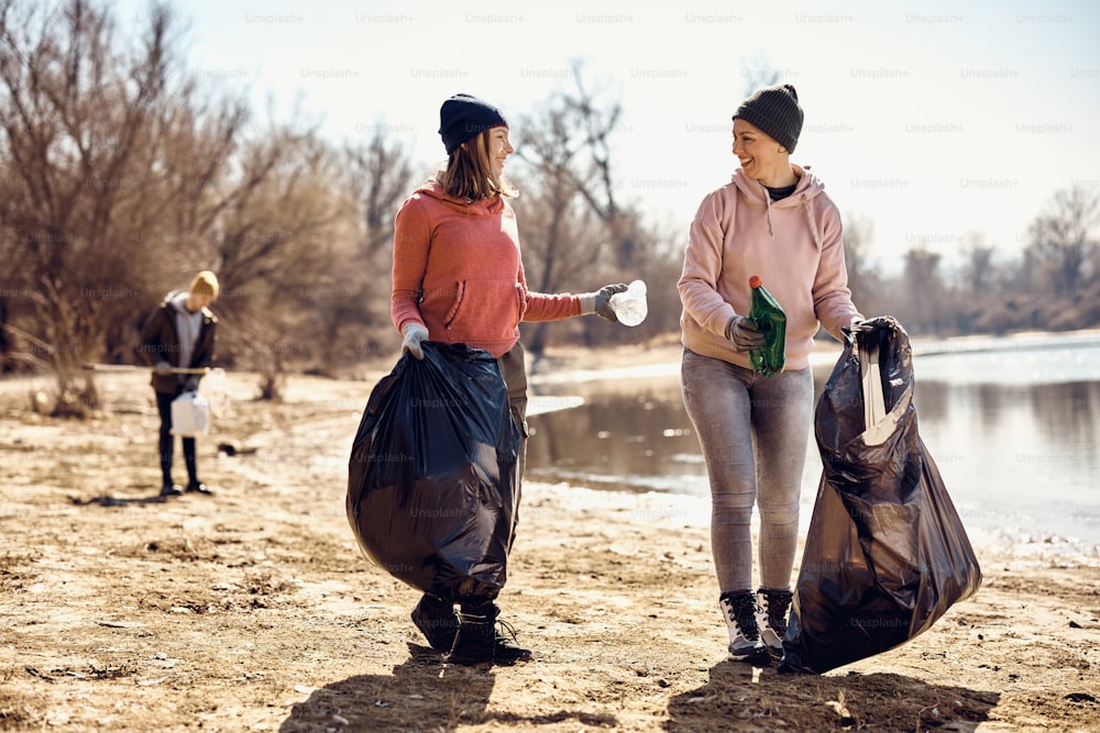 Happy female volunteers communicating while collecting the trash on the beach.