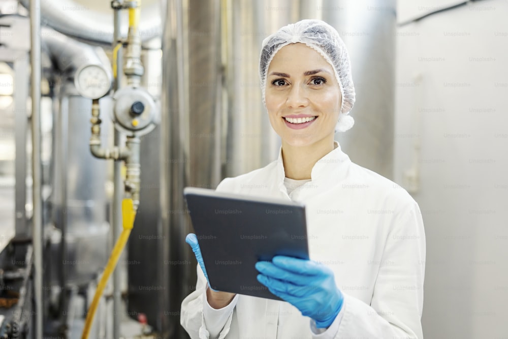 A female milk plant supervisor scrolling on tablet and smiling at the camera.