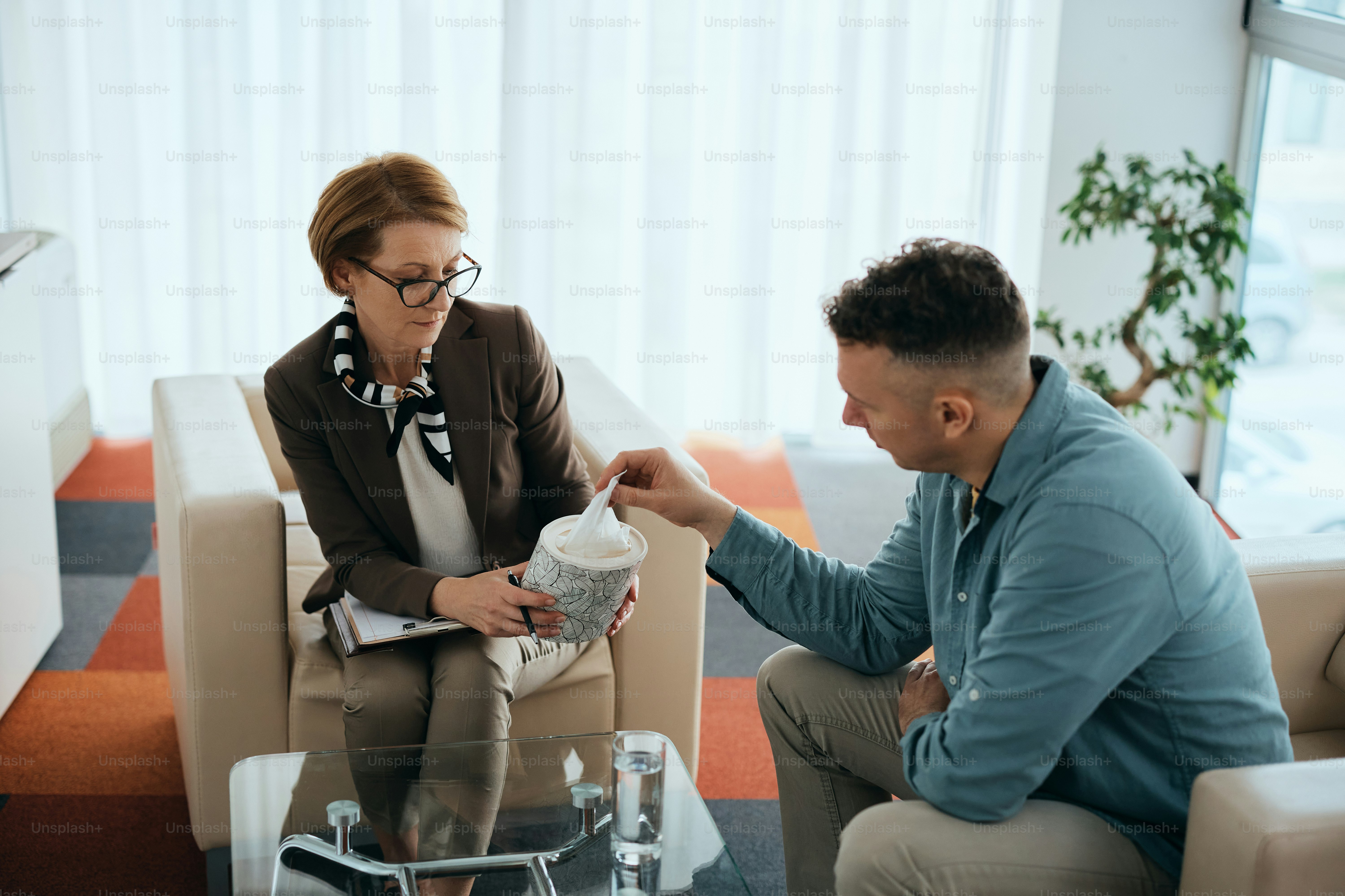 Reife Psychiaterin, die ihrer Patientin während der therapeutischen Sitzung Gewebe anbietet.