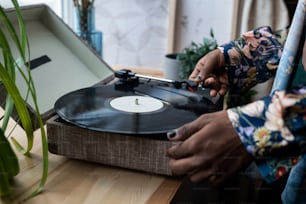 Hände eines jungen schwarzen Mannes mit Nagellack, der Schallplatte auf Nadelspieler legt, der auf Holzfensterbank steht, bevor er Retro-Musik hört