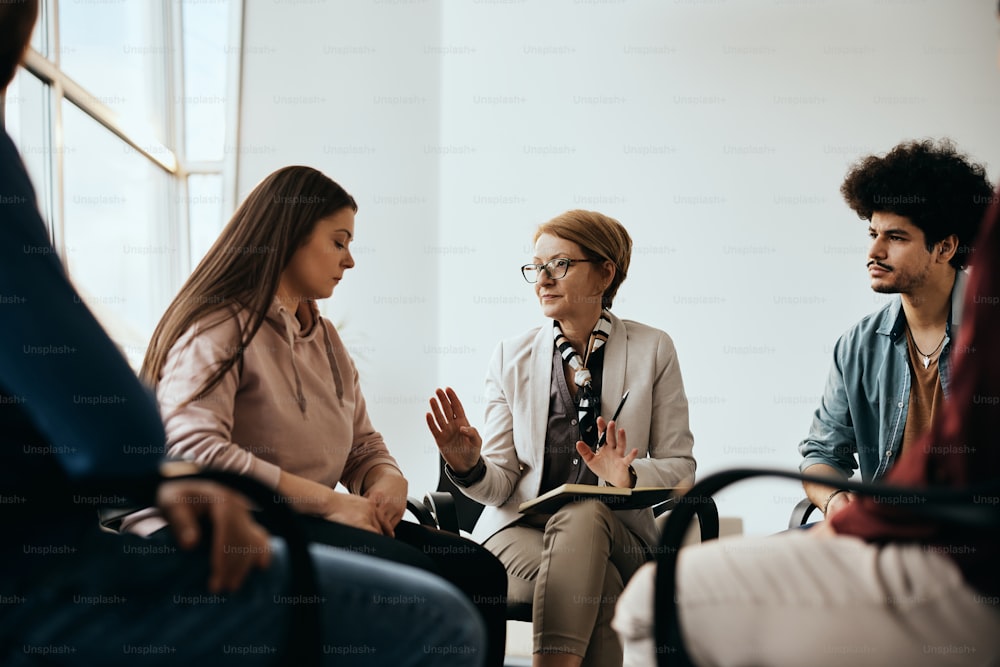 Mature mental health professional communicating with group of people during counseling at community center.
