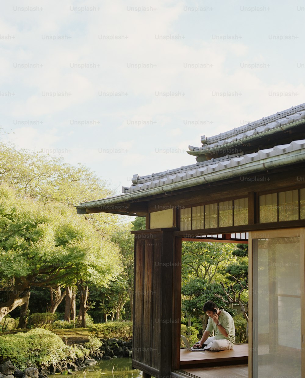 Young man using cell phone and laptop in room overlooking garden