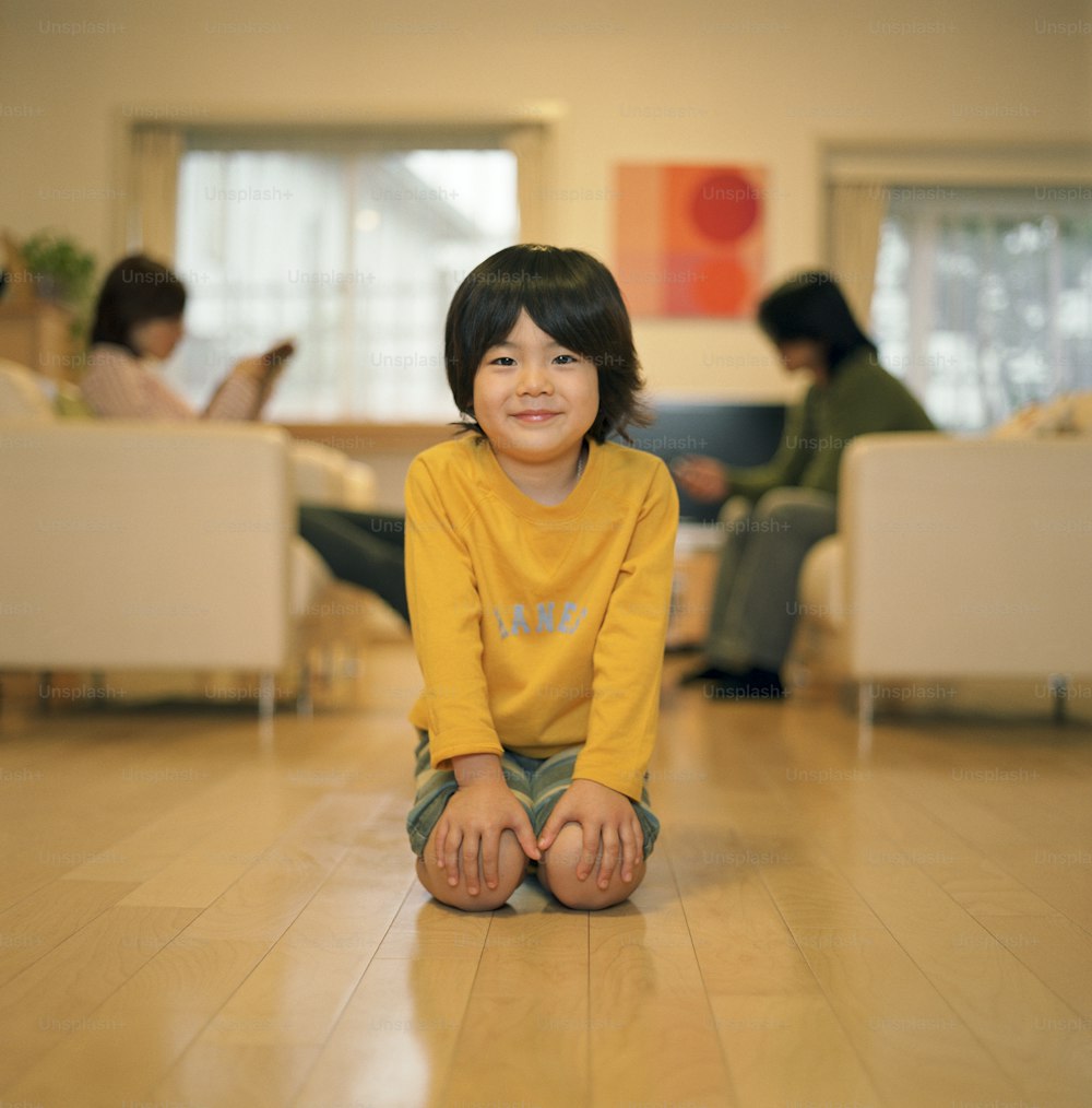 Boy (4-6) kneeling on floor, smiling, parents sitting in background