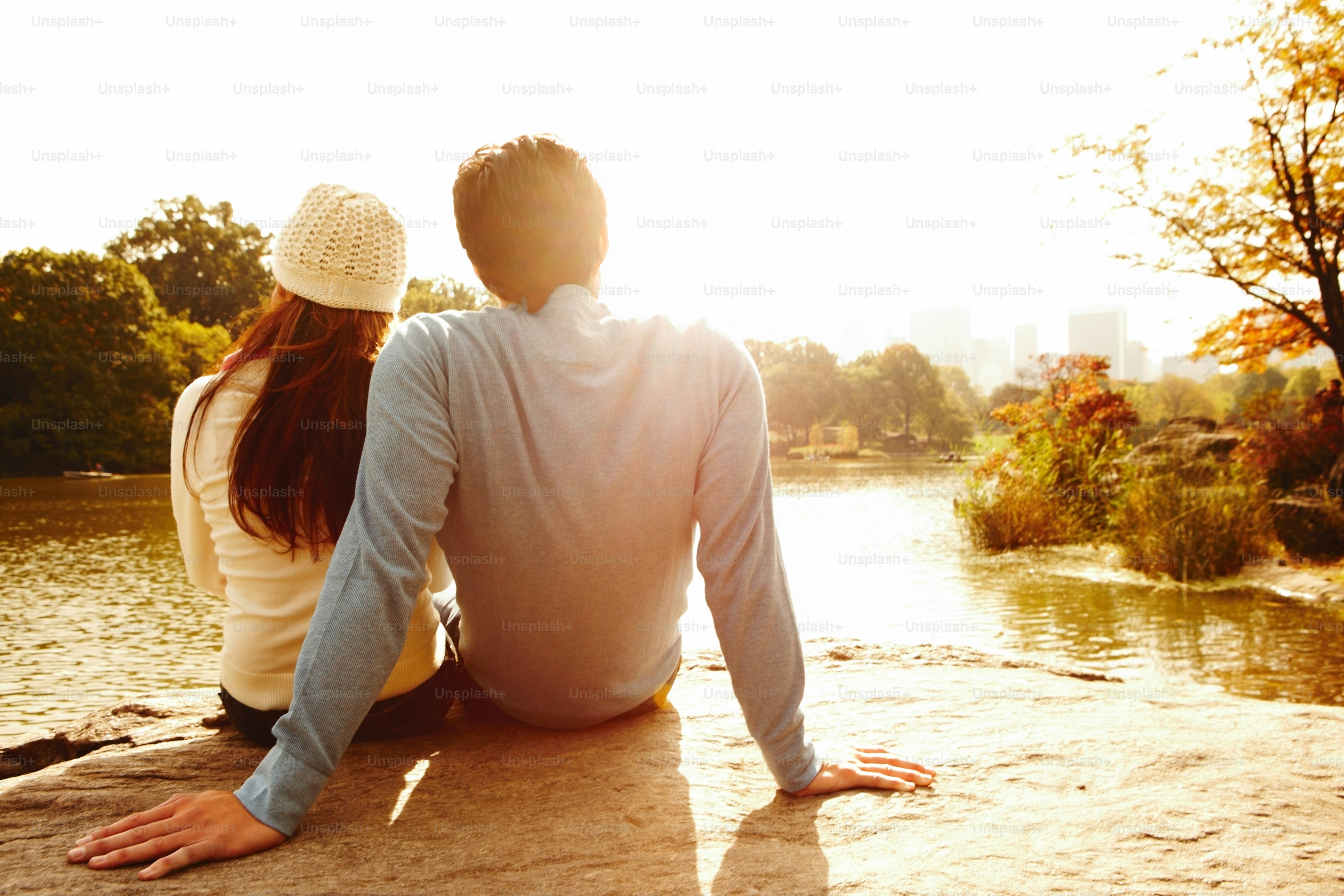 A man and a woman sitting on the edge of a lake photo – Sunset Image on ...