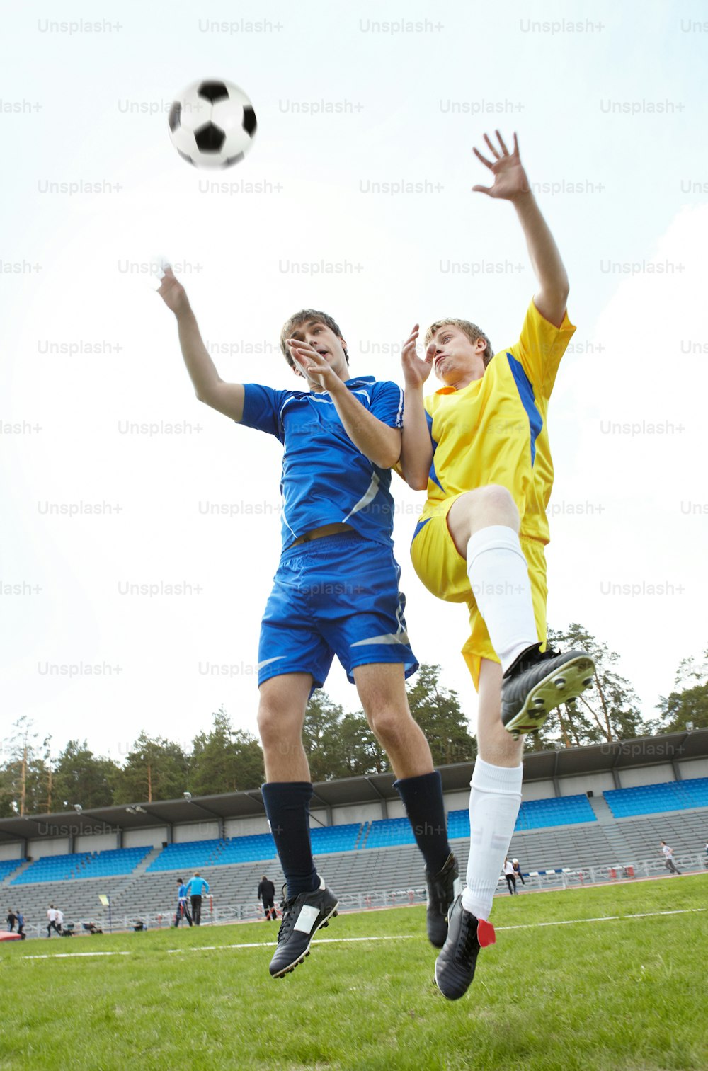 Two footballers jumping and looking at ball on grass-field during game