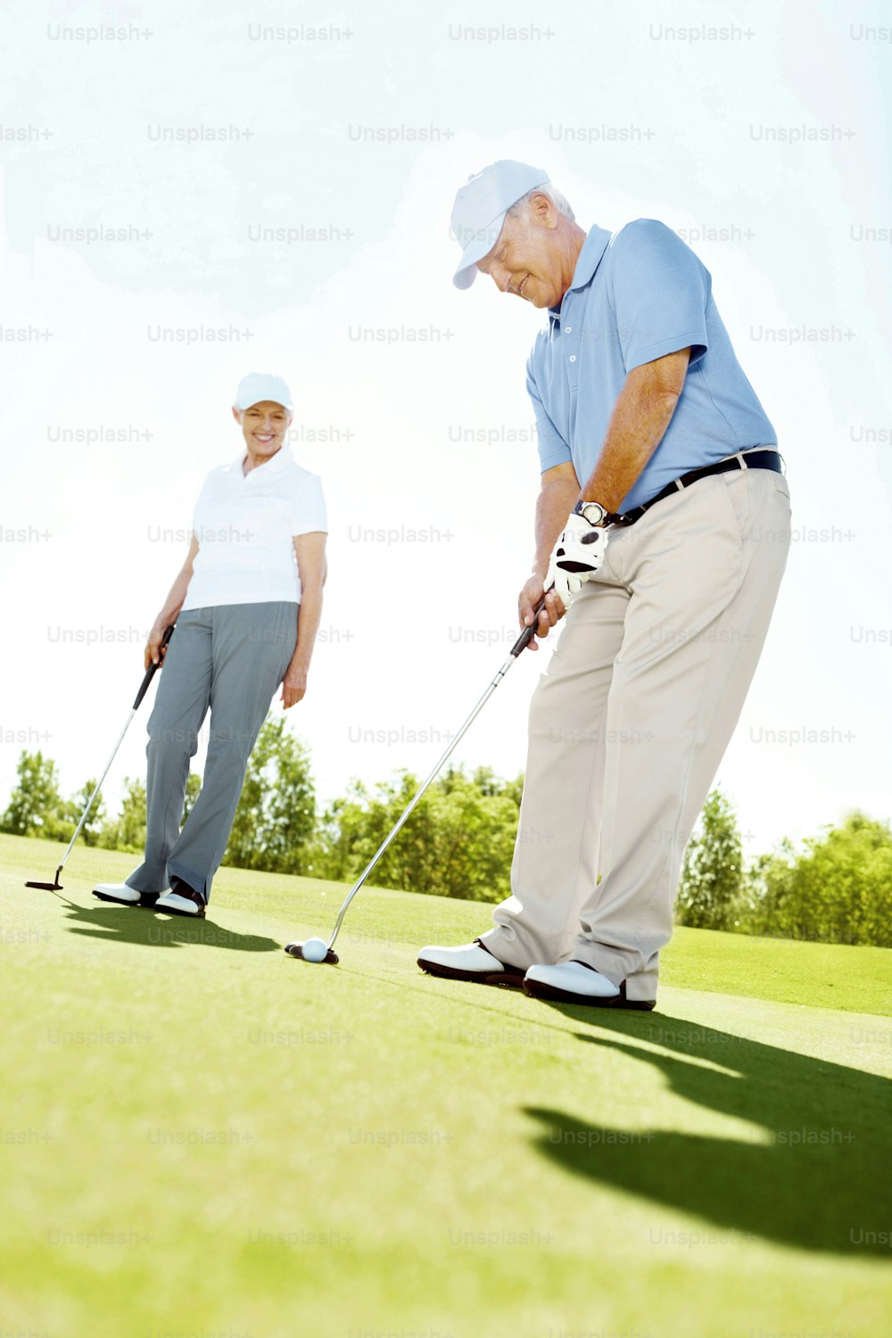 A senior woman watches as her husband putts for the hole
