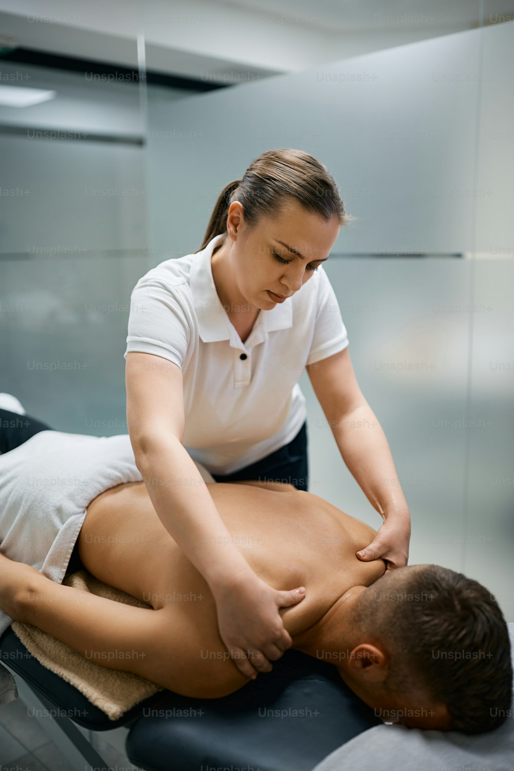 Kinésithérapeute massant les épaules d’un homme pendant la physiothérapie sportive.