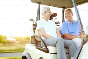 A senior couple sitting in a golf cart on a crisp morning at sunrise