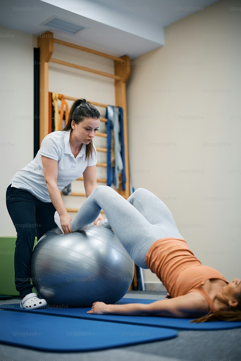 Physiotherapeut mit Fitnessball während der therapeutischen Behandlung mit Patientin im Fitnessstudio.