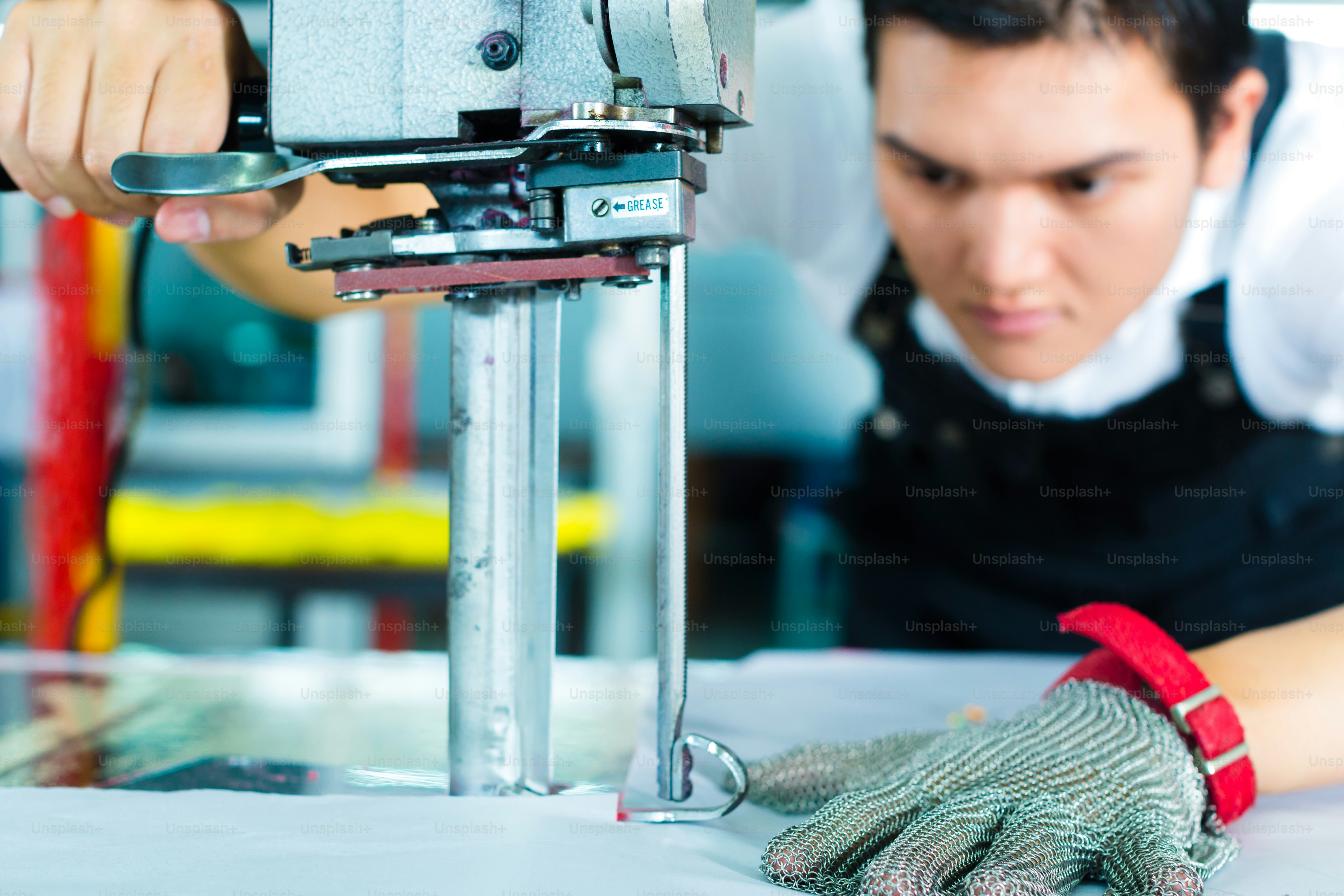 worker using a cutter - a large machine for cutting fabrics- in a Chinese textile factory, he wears a chain glove
