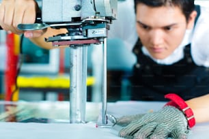 中国の繊維工場でカッター(生地を裁断するための大型機械)を使用する労働者は、チェーングローブを着用しています