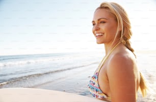 A beautiful surfer girl standing on a beach and smiling with her surfboard under her arm