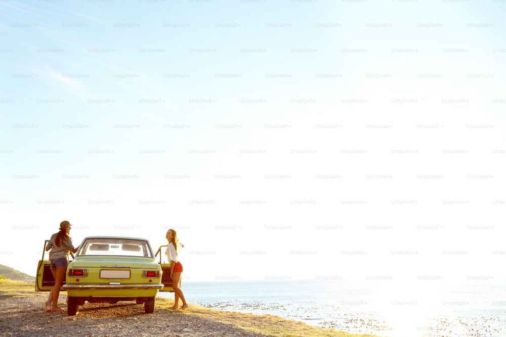 Two young woman outside of their car at the beach after a roadtrip