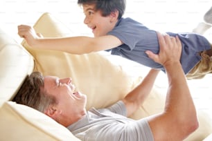 Un padre levantando a su hijo en el aire mientras está acostado en el sofá del salón