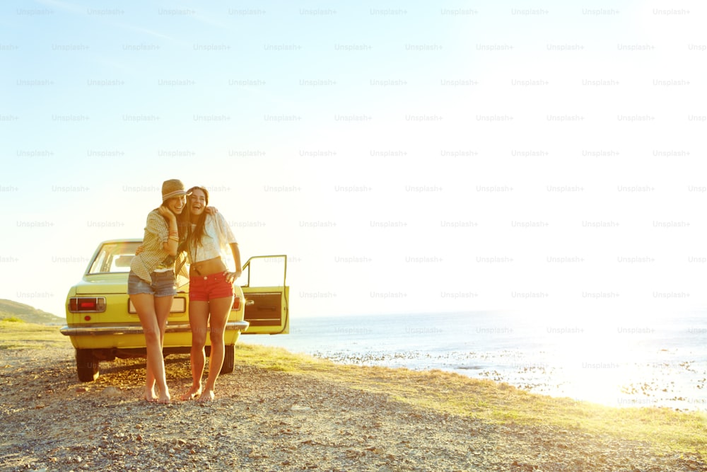 Two young woman outside of their car at the beach after a roadtrip