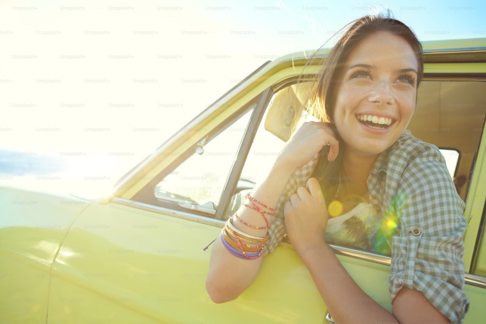 Lächelnde junge Frau sitzt in einem geparkten Auto mit Meerblick