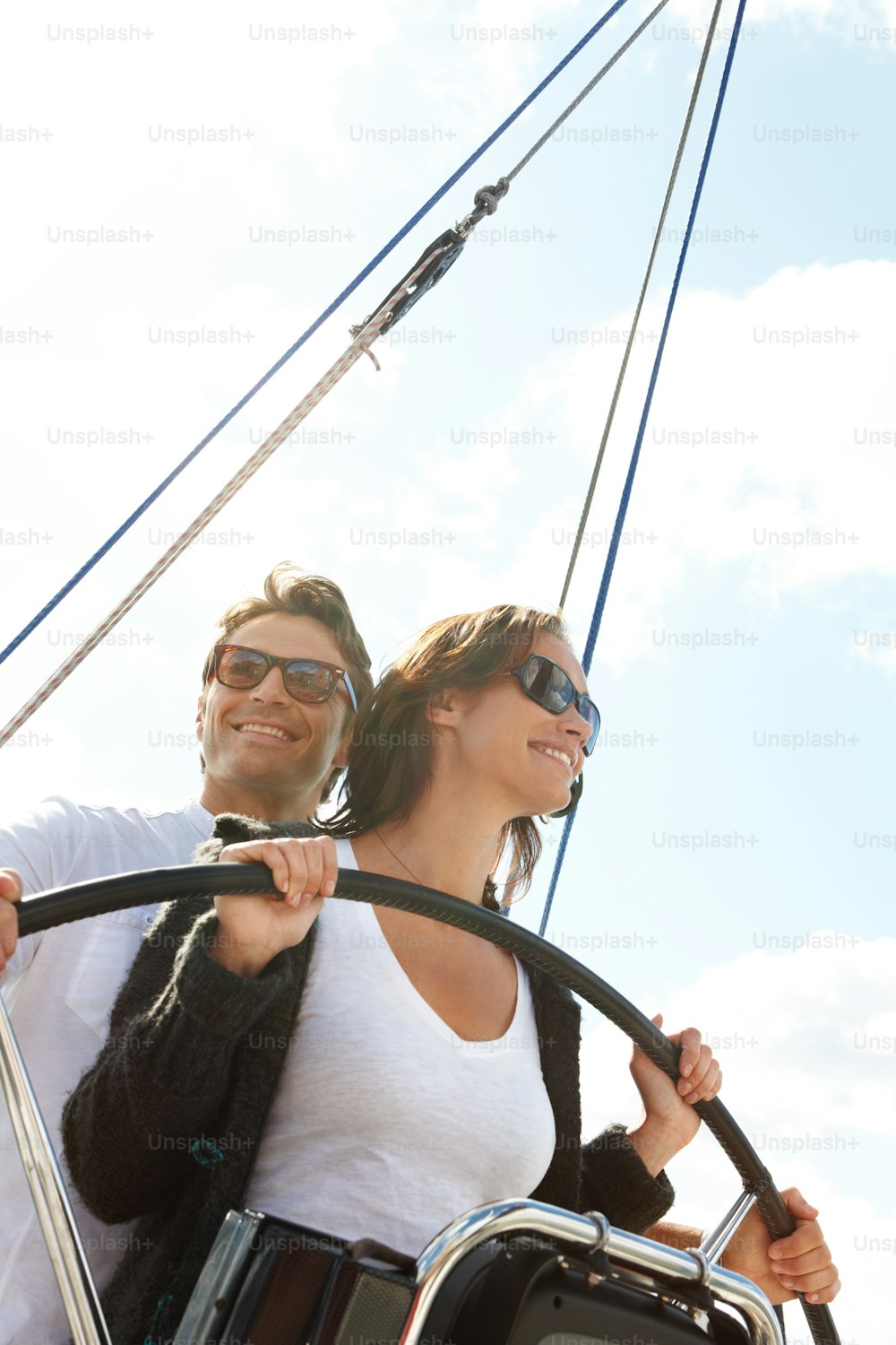 Una pareja joven y atractiva sonriendo mientras está de pie al timón de un barco