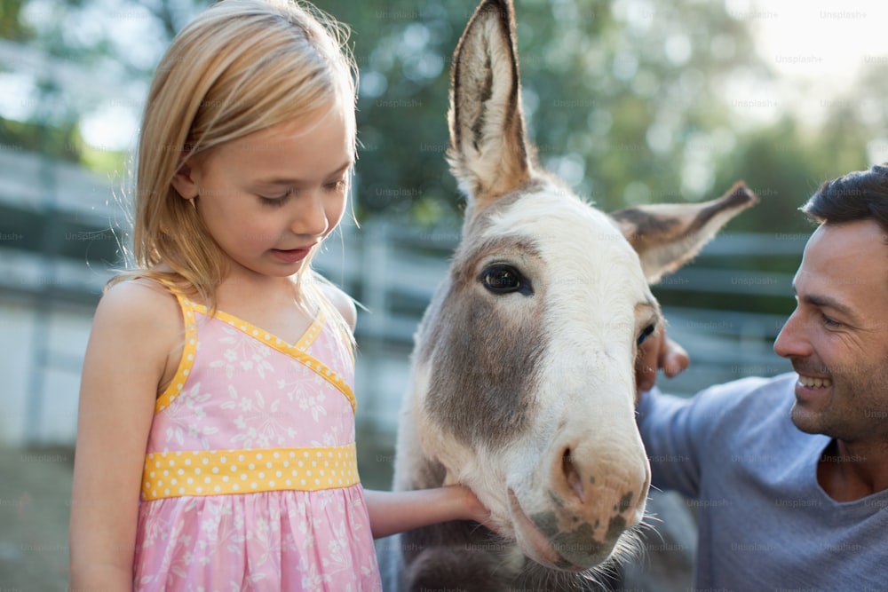 Ein Mann und ein kleines Mädchen streicheln einen Esel