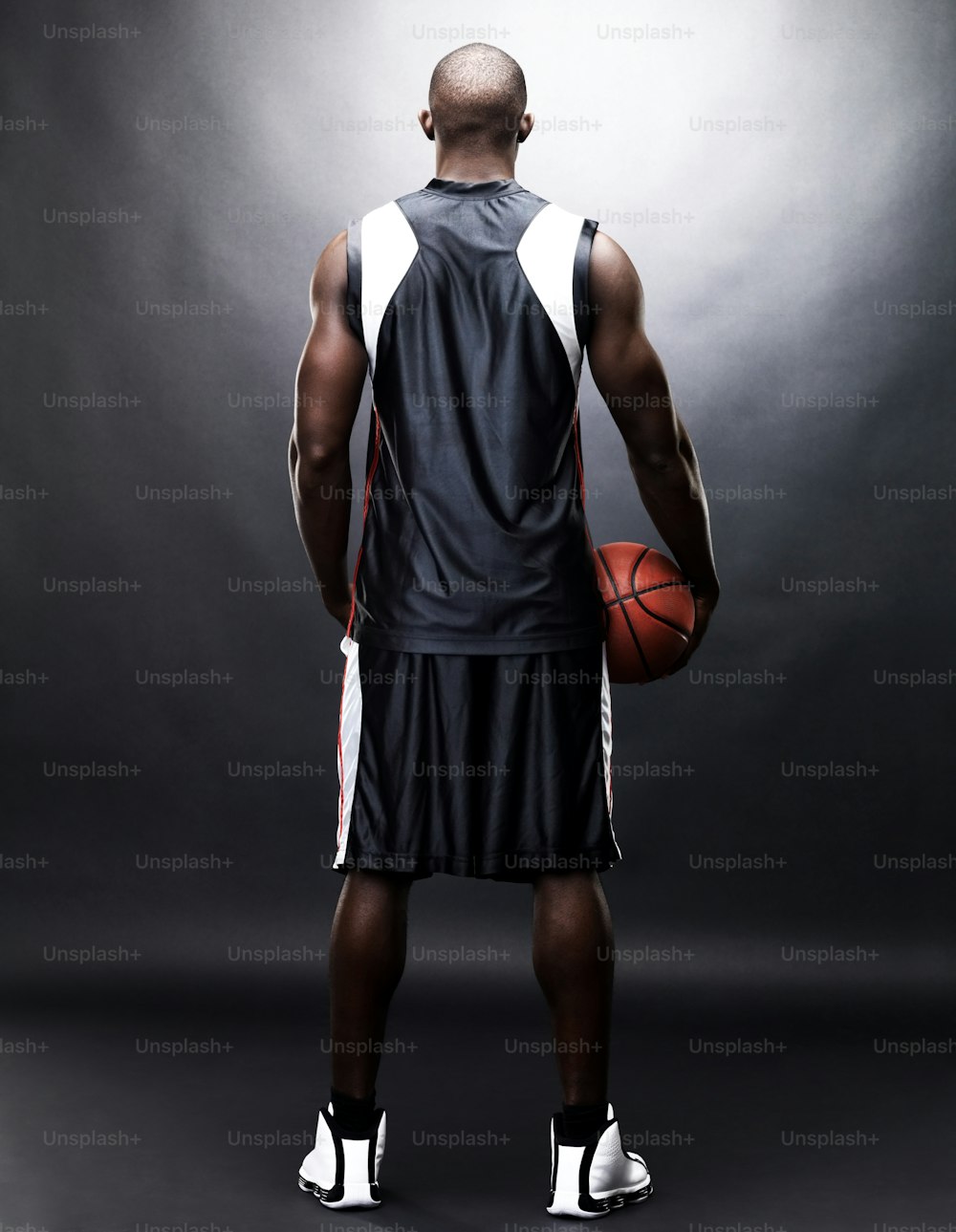 a man holding a basketball standing in front of a dark background
