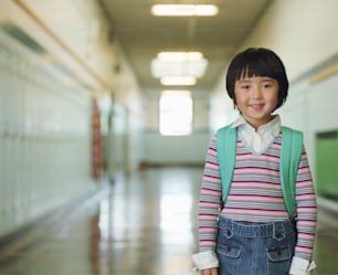 Une petite fille debout dans un couloir avec un sac à dos