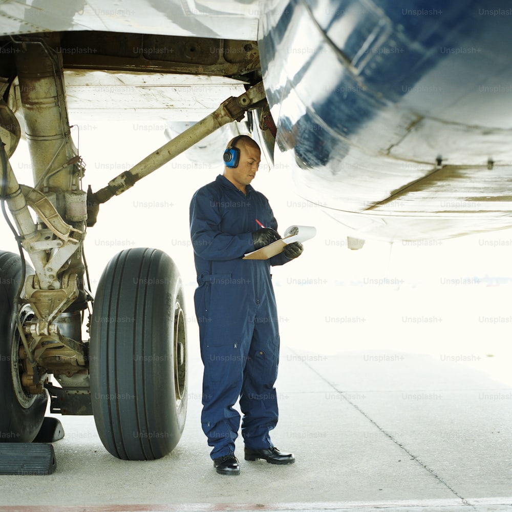 a man in blue overalls standing next to an airplane