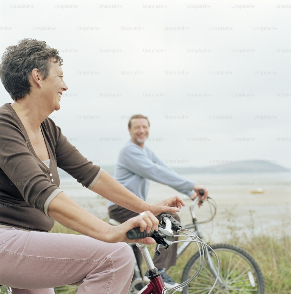 um homem e uma mulher andando de bicicleta na praia