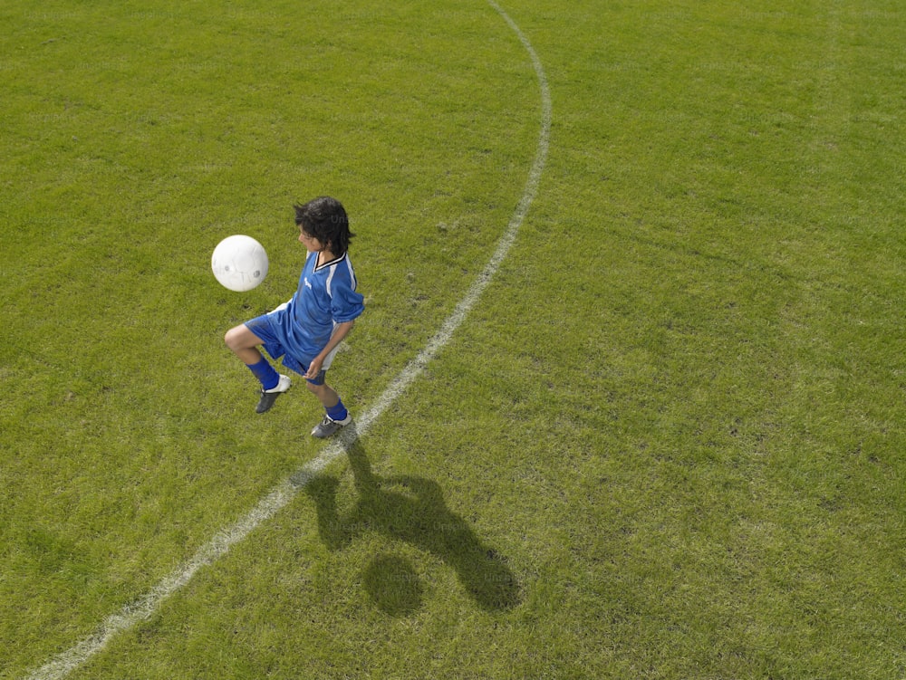 a young boy kicking a soccer ball across a field
