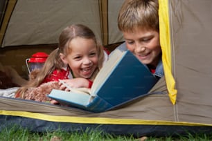a couple of kids laying in a tent reading a book