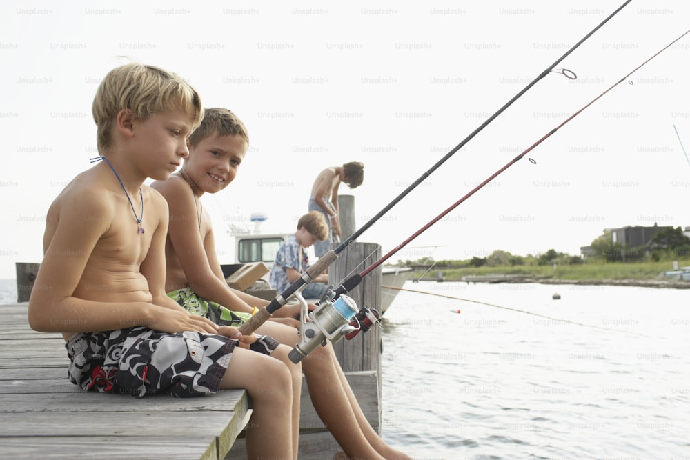 two young boys sitting on a dock fishing