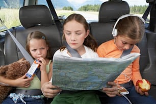 three girls sitting in the back of a car looking at a map