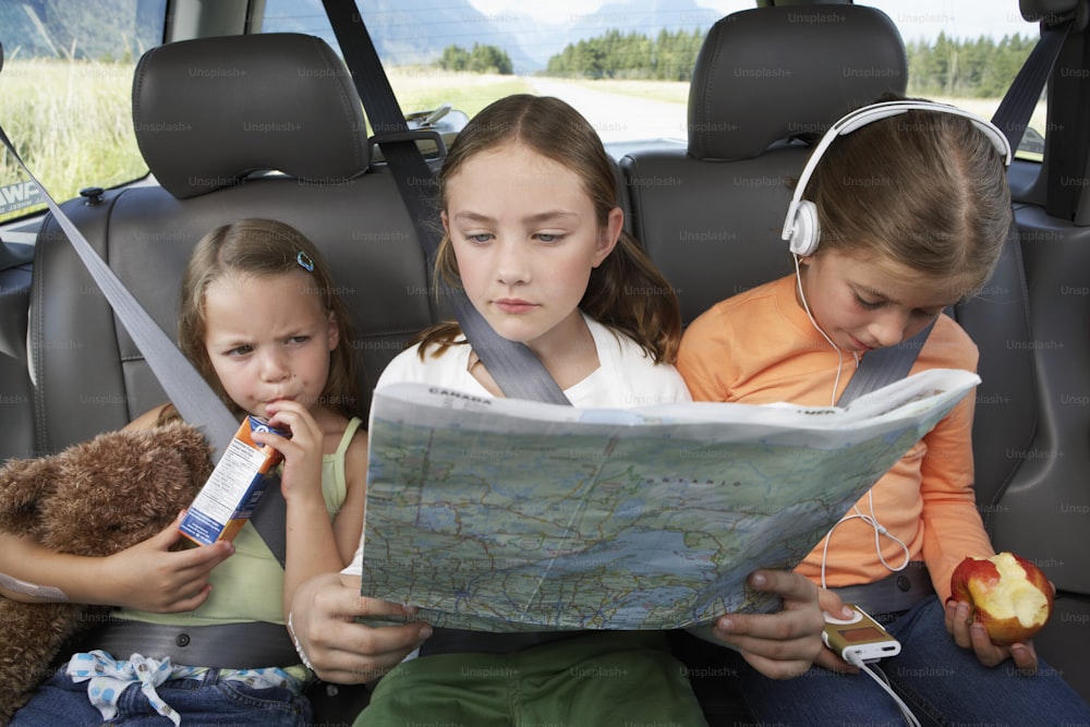 three girls sitting in the back of a car looking at a map