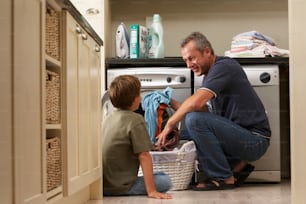 a man and a boy are doing laundry in a kitchen