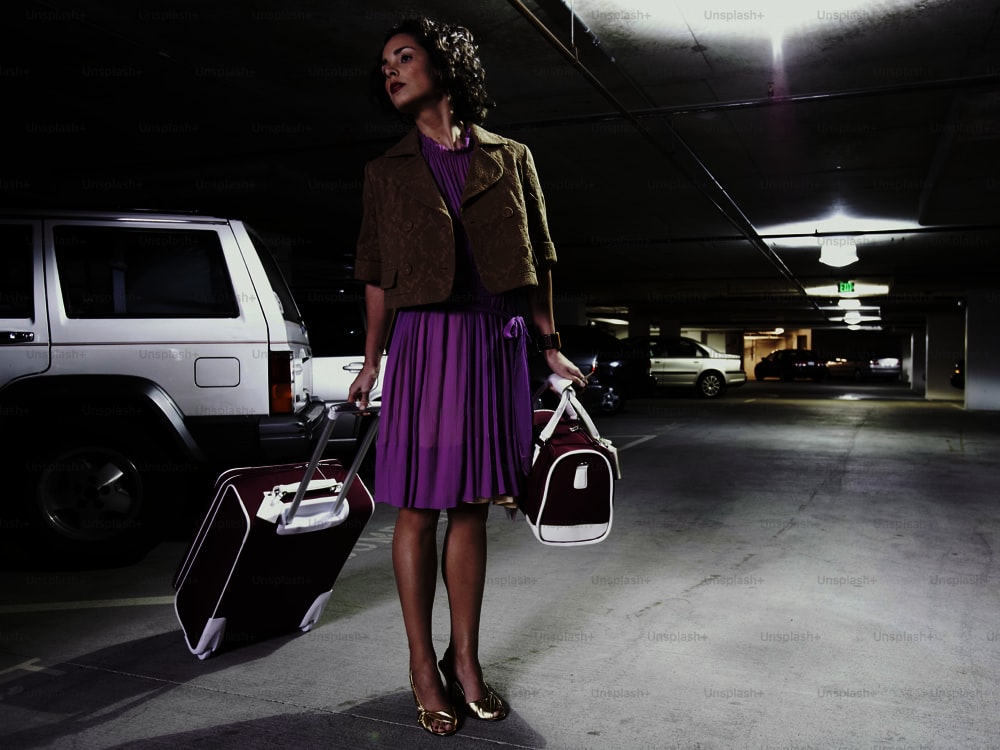 a woman in a parking garage holding two suitcases