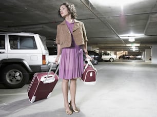 a woman in a parking garage holding two suitcases