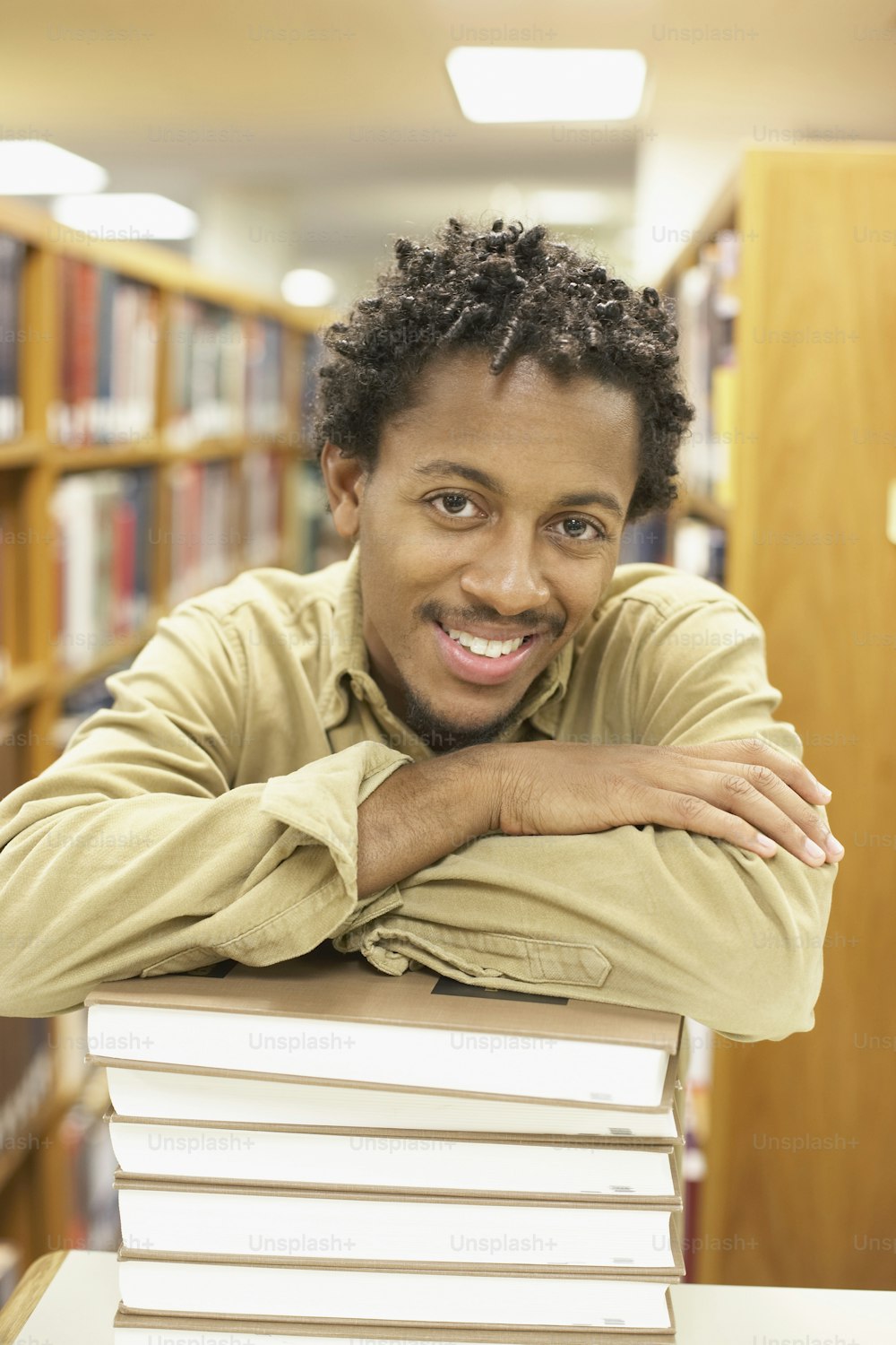 Ein Mann, der sich in einer Bibliothek auf einen Stapel Bücher stützt