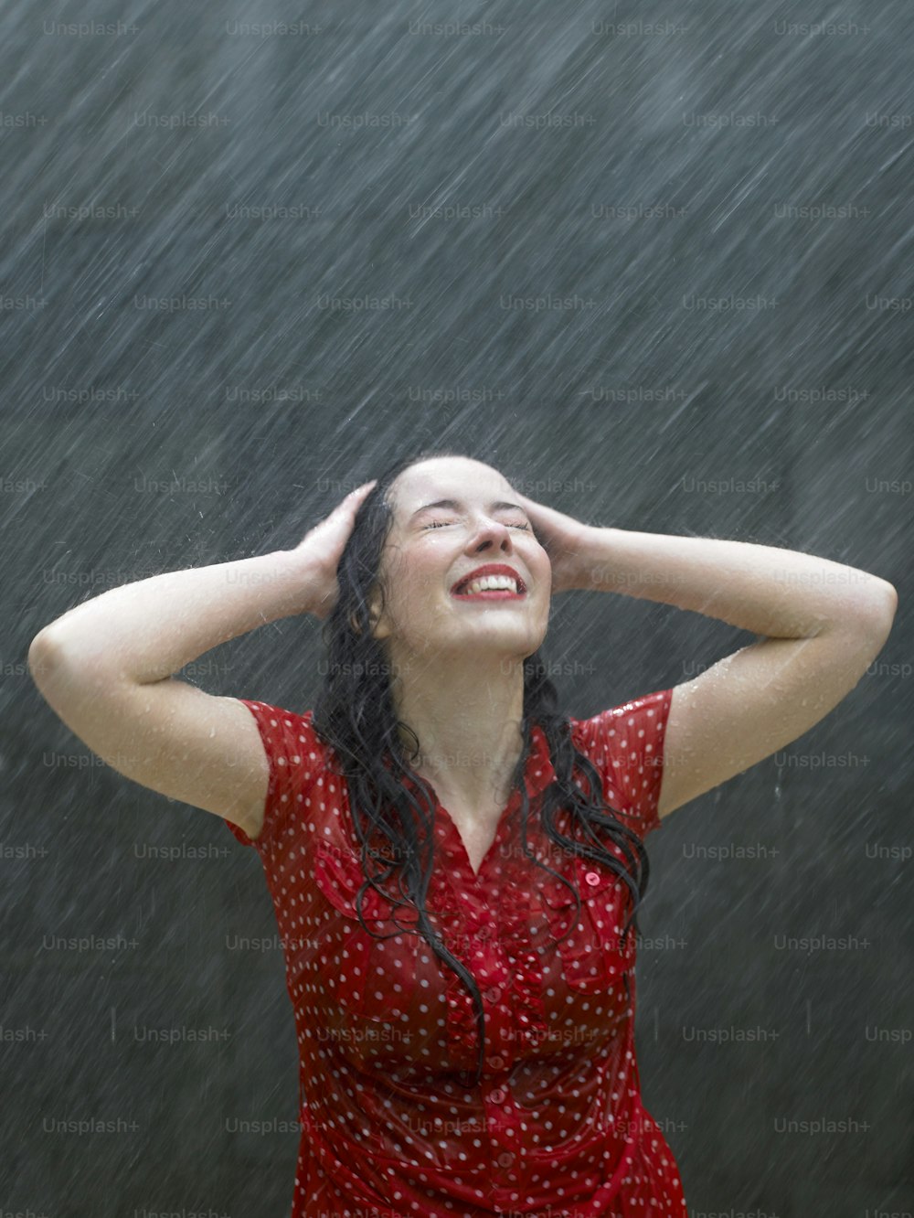 Una mujer parada bajo la lluvia con las manos en la cabeza