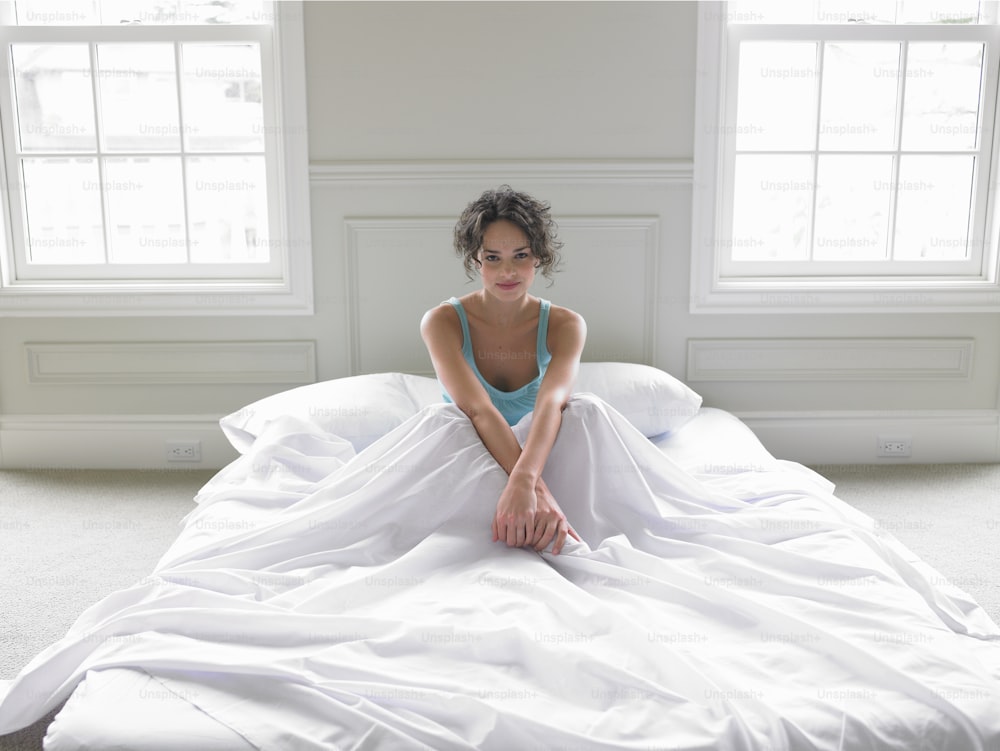 a woman sitting on top of a bed covered in white sheets