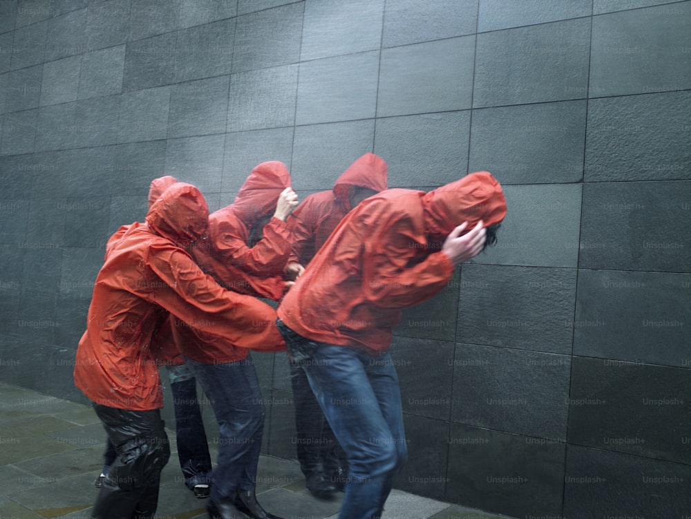 um grupo de pessoas com capas de chuva vermelhas encostadas a uma parede