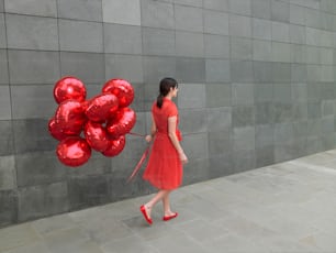 a woman in a red dress holding a bunch of red balloons
