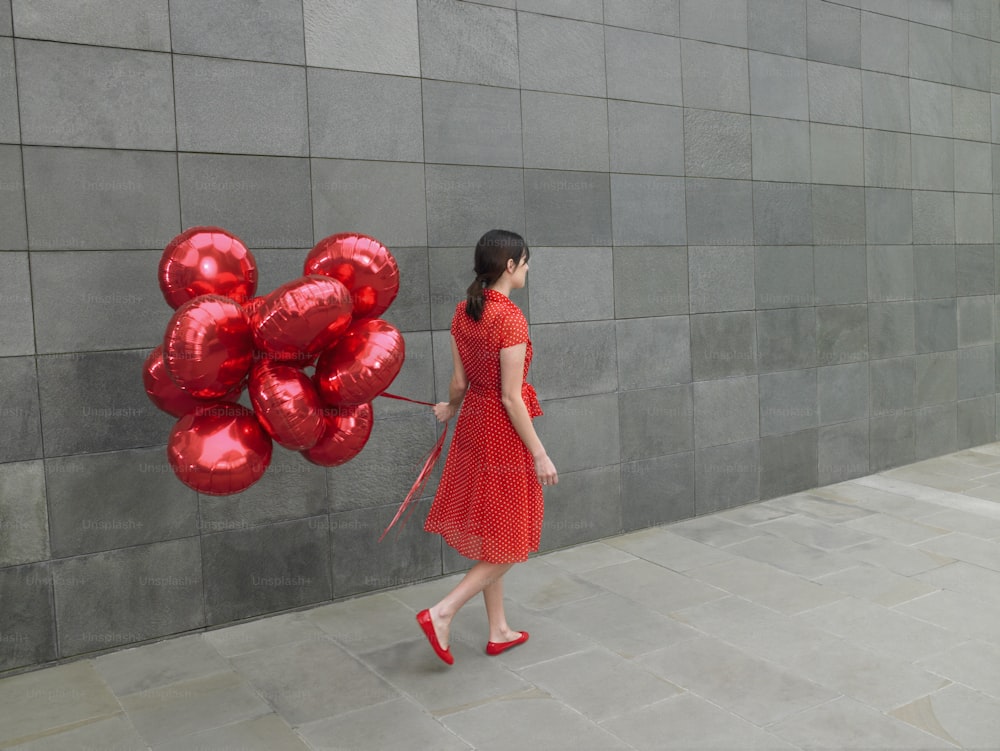 a woman in a red dress holding a bunch of red balloons