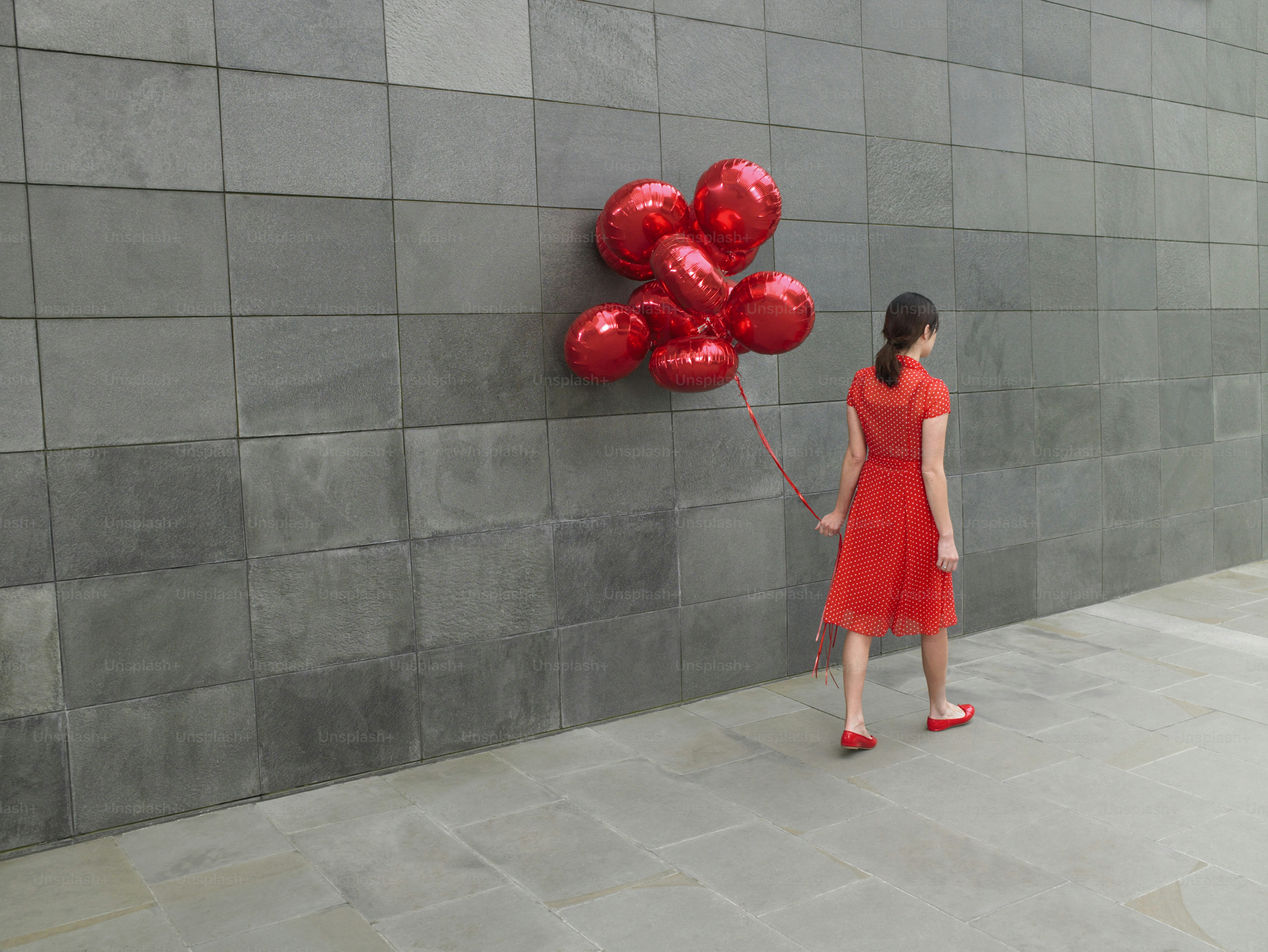 a woman in a red dress holding a bunch of red balloons