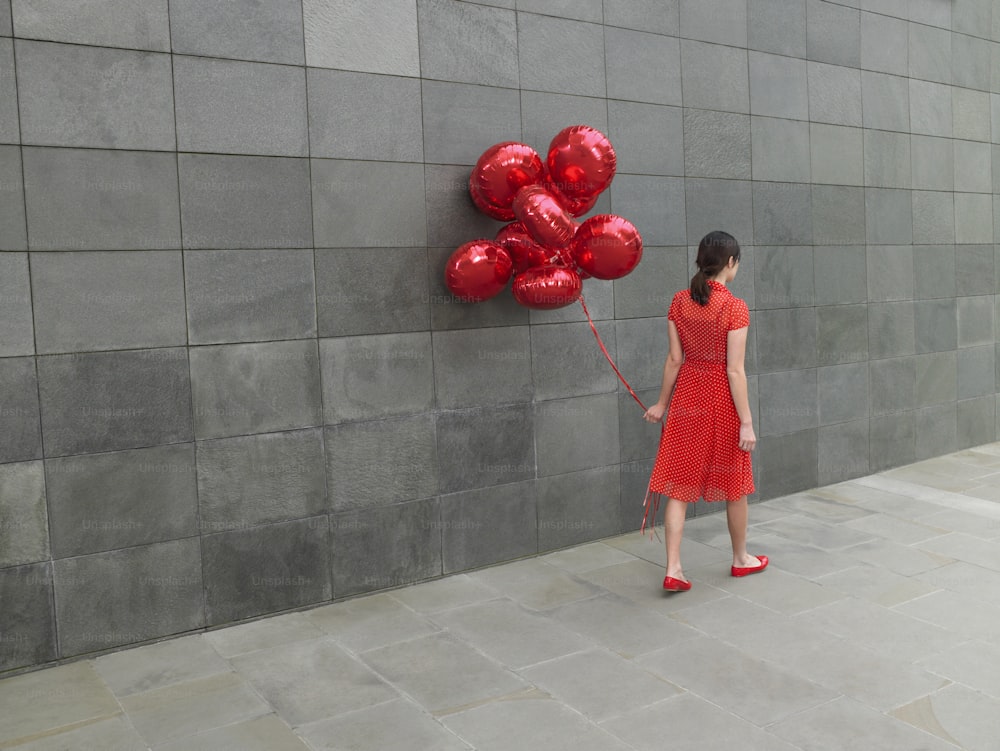 uma mulher em um vestido vermelho segurando um monte de balões vermelhos