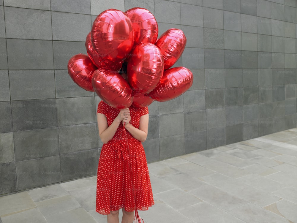 a woman holding a bunch of red balloons