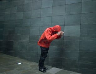 a man in a red jacket leaning against a wall