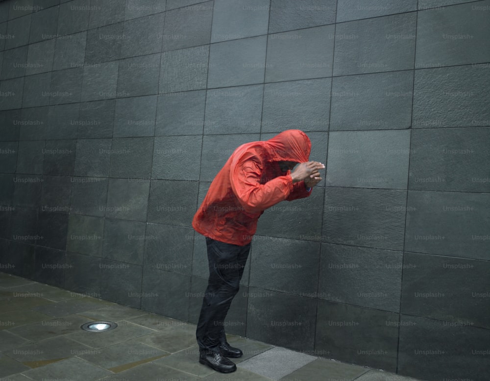 a man in a red jacket leaning against a wall