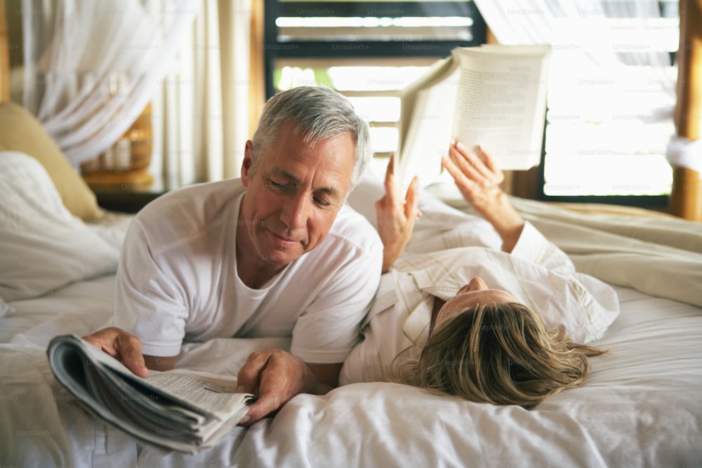 a man and a woman laying in bed reading a book
