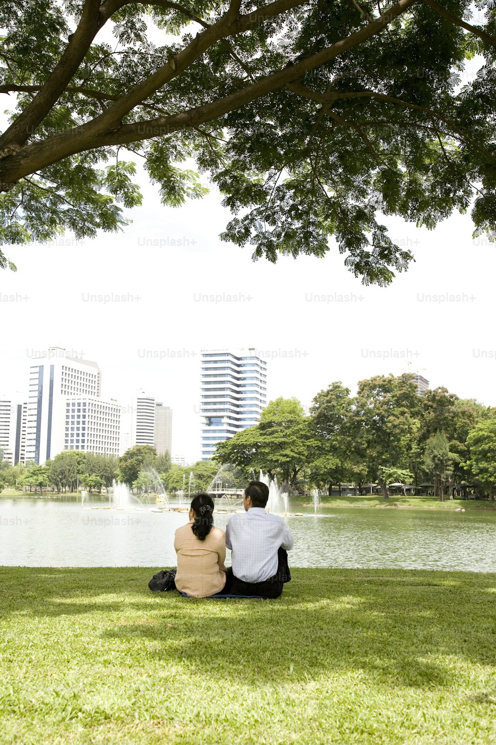 a man and a woman sitting on the grass near a lake