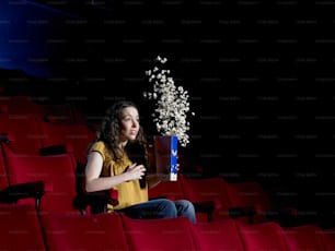 uma mulher sentada em um teatro segurando uma caixa de pipoca